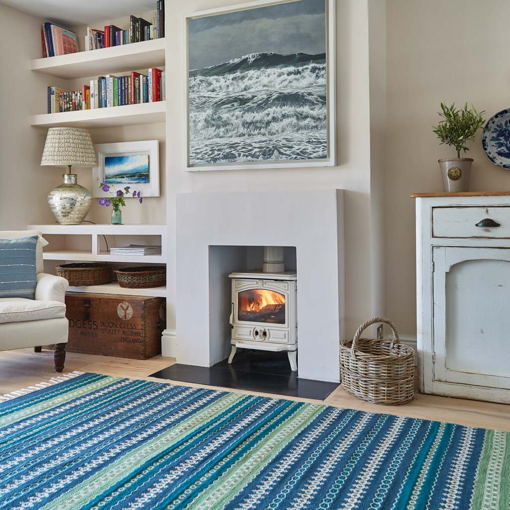 A colorful striped rug with green and blue stripes displayed in a room with a fireplace and wooden furniture.