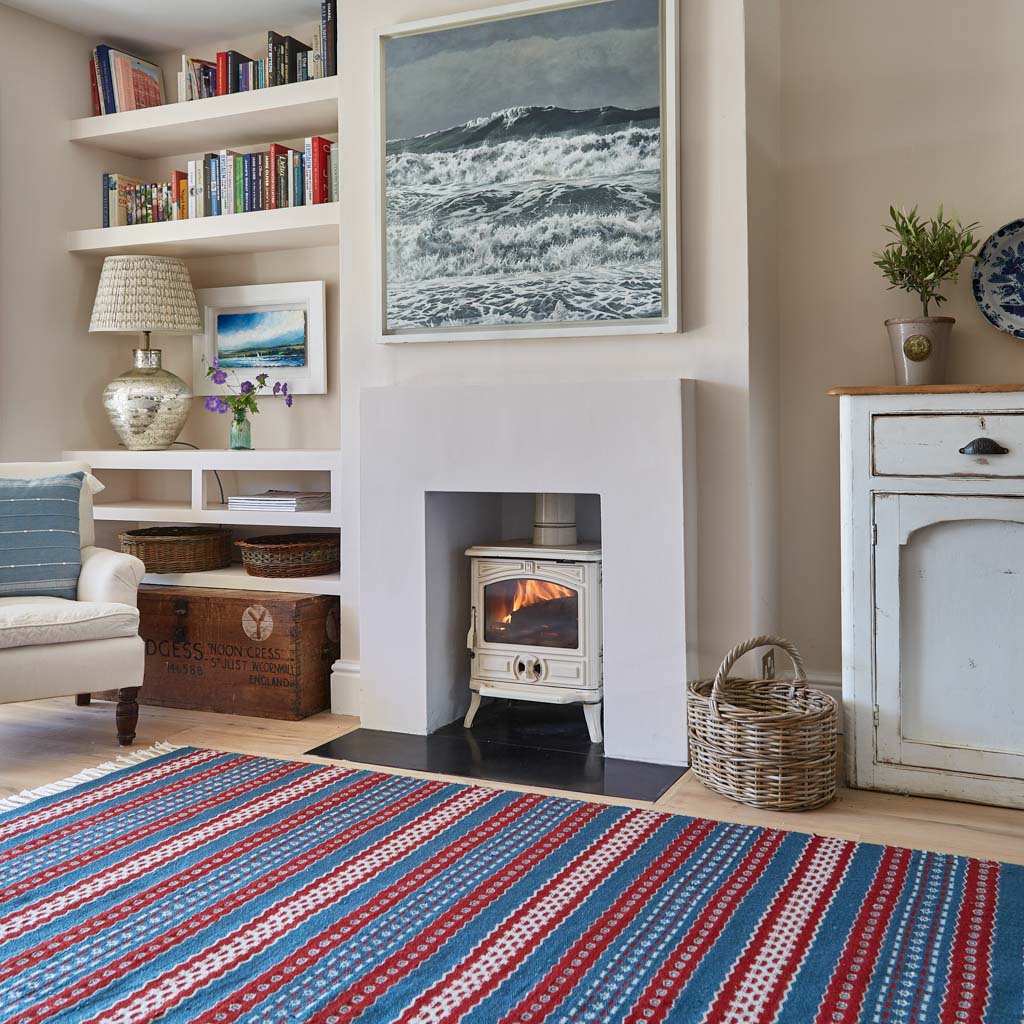 A red and blue striped rug with a geometric pattern laid out on a wooden floor, next to a fireplace 