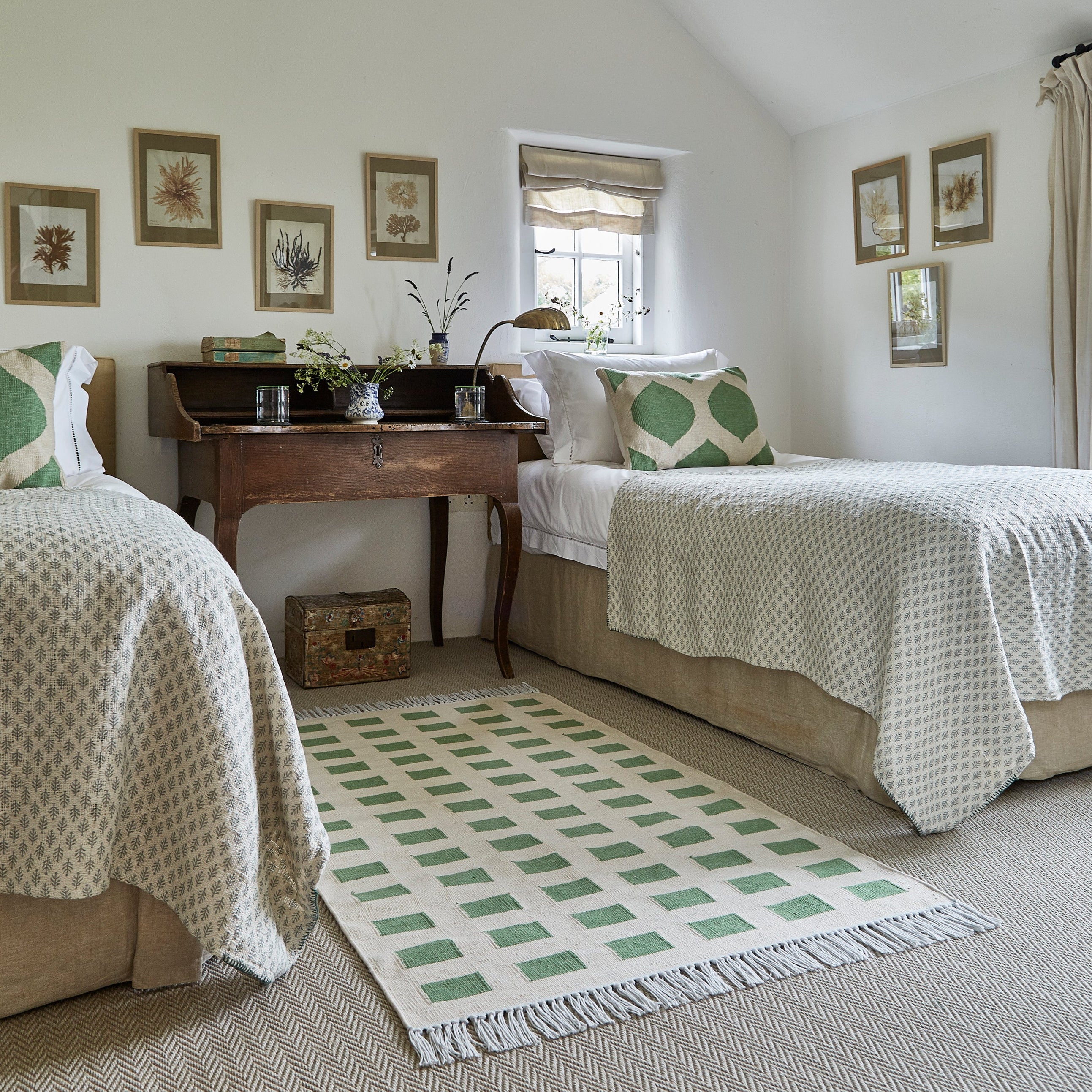 Two beds in a bedroom with a checkered rug and decorative pillows.