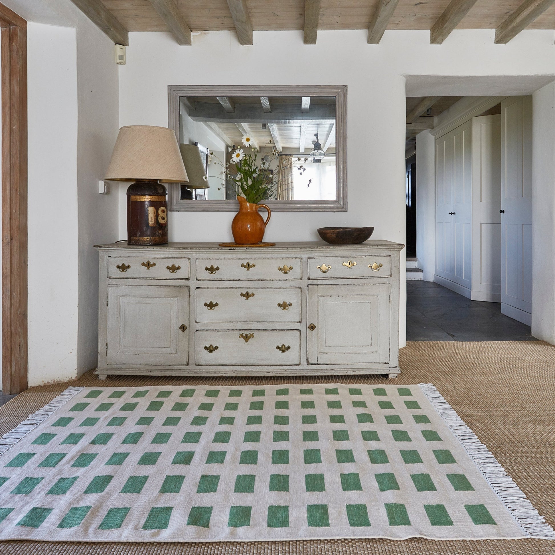 Living room with a checkered rug, white dresser, and decorative items.
