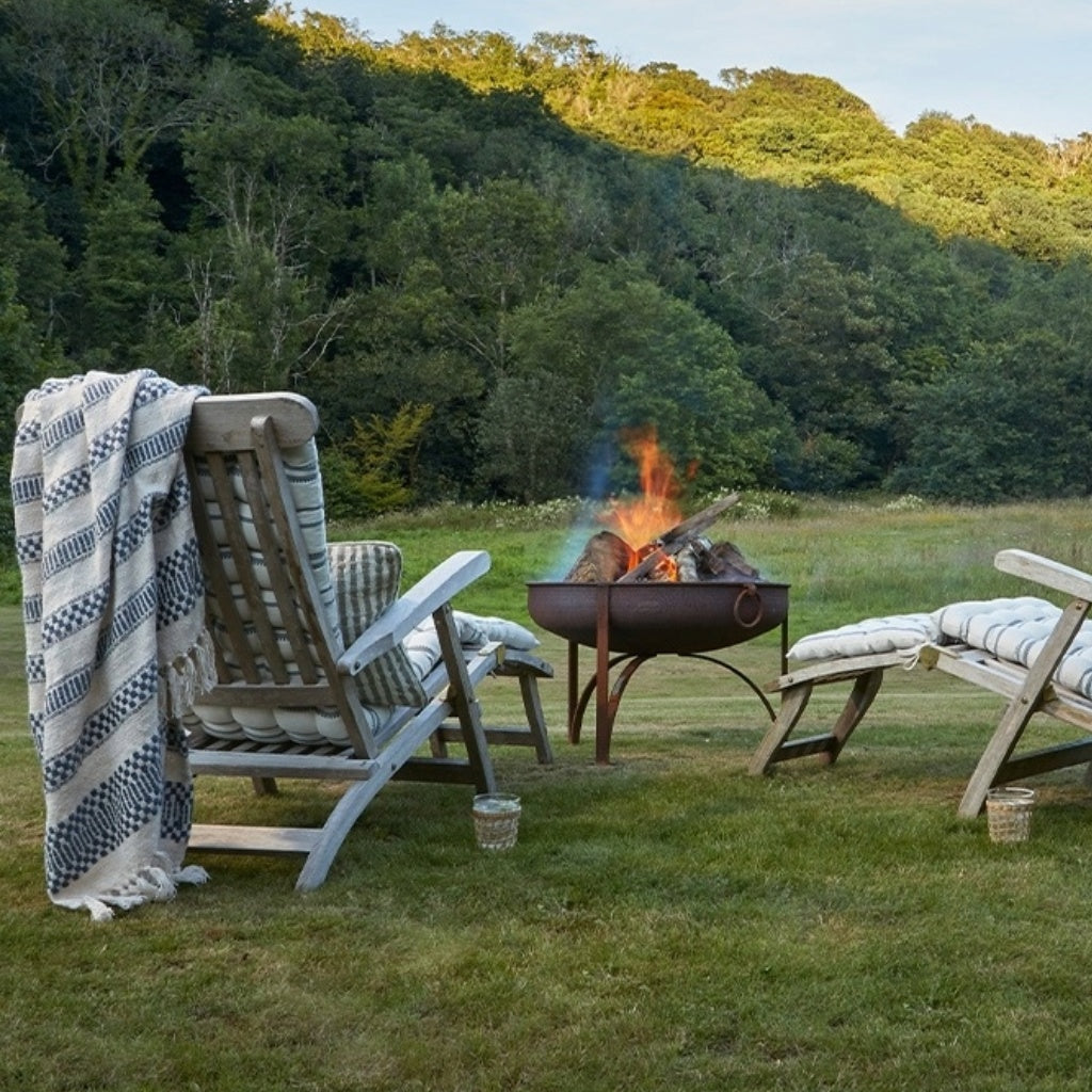 Outdoor setting with deck chairs, and Weaver Green Blankets, throws and cushions and a fire pit in a forested area.