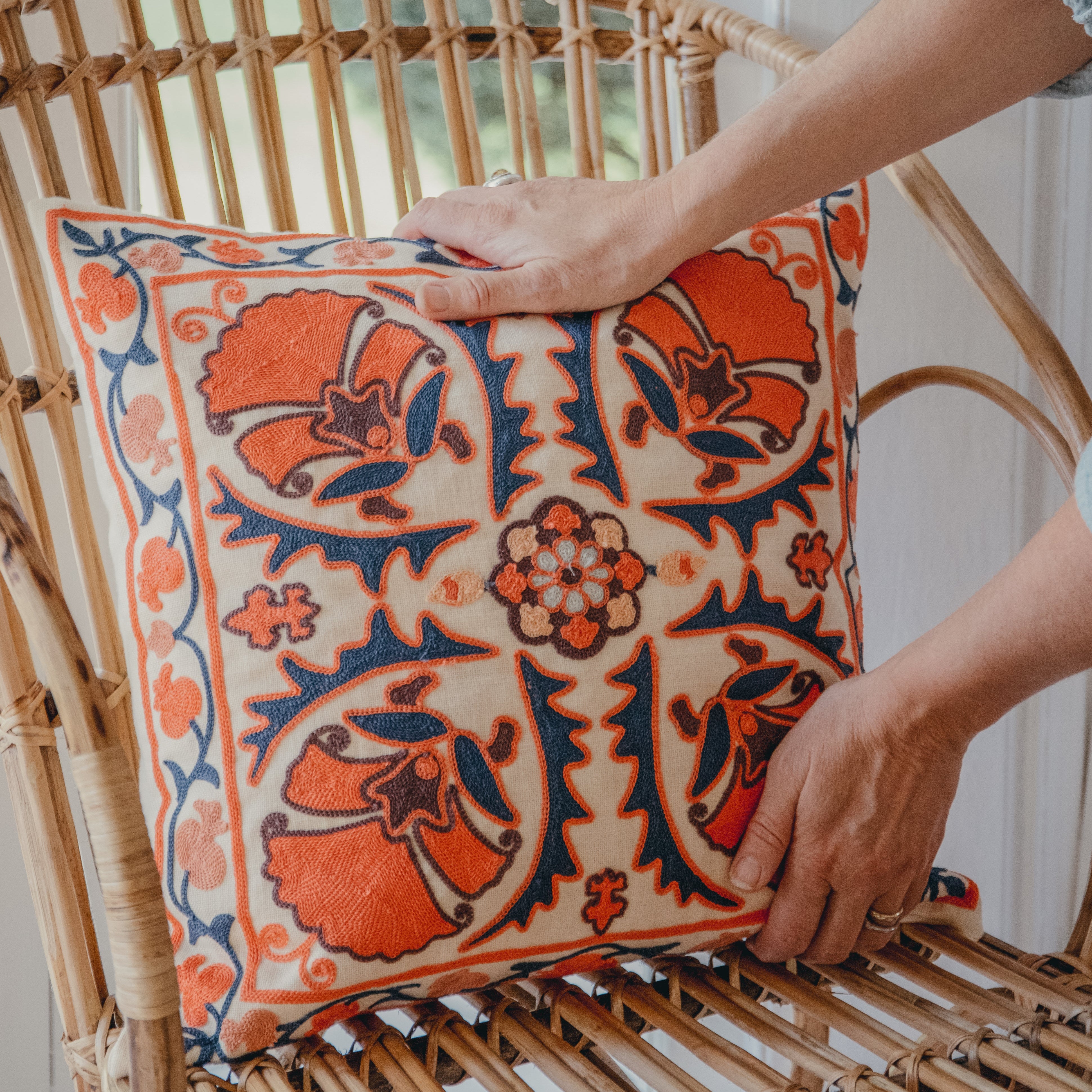 Person arranging a decorative pillow on a wicker chair with a blurred outdoor background