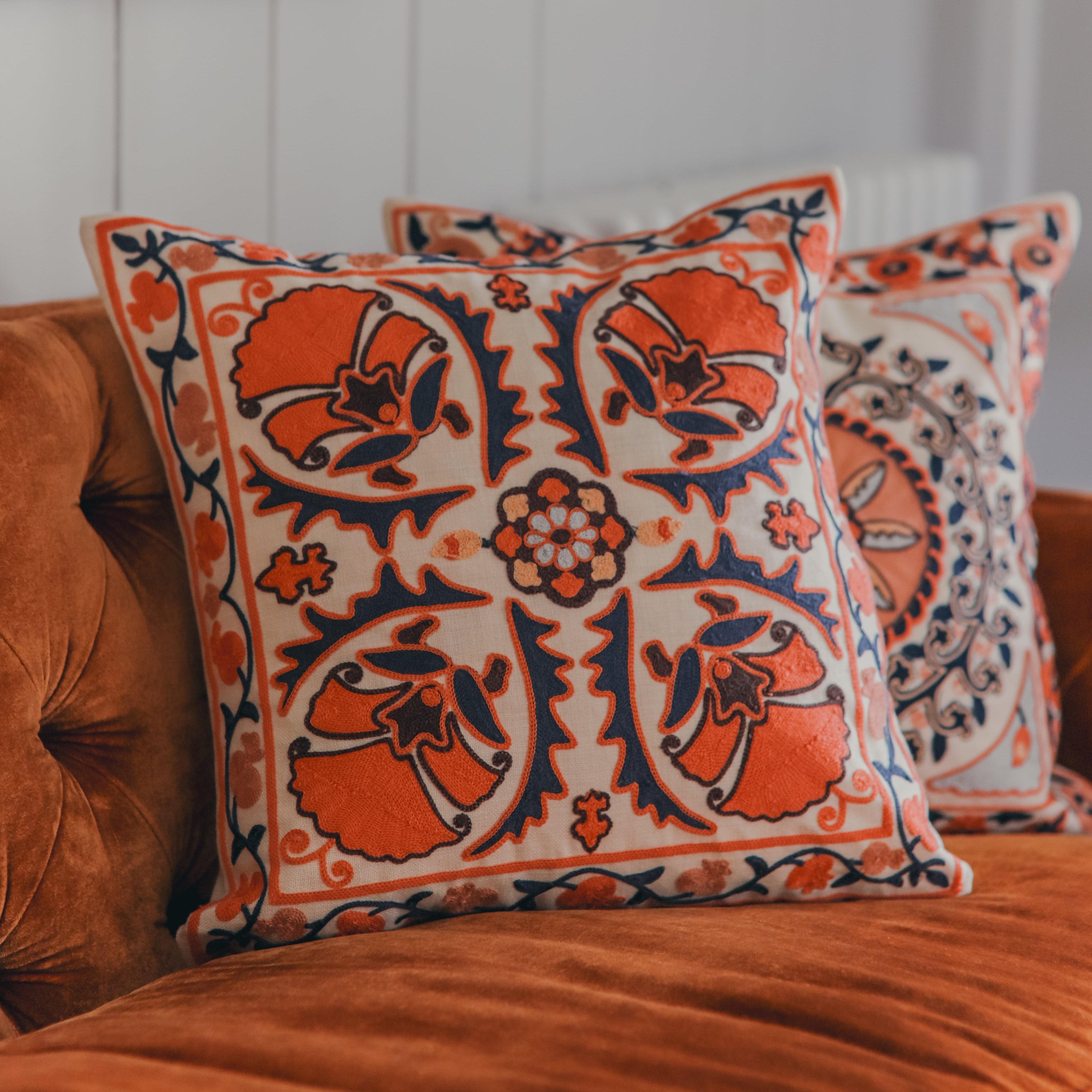 Decorative pillows with orange and white patterns on a brown couch.
