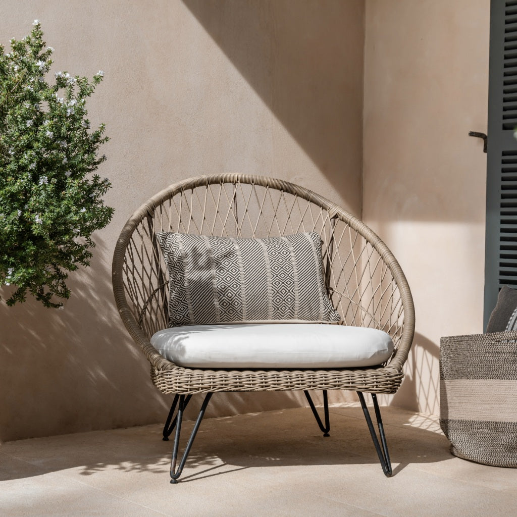 Wicker chair with cushions on a patio with a neutral wall and plant in the background.