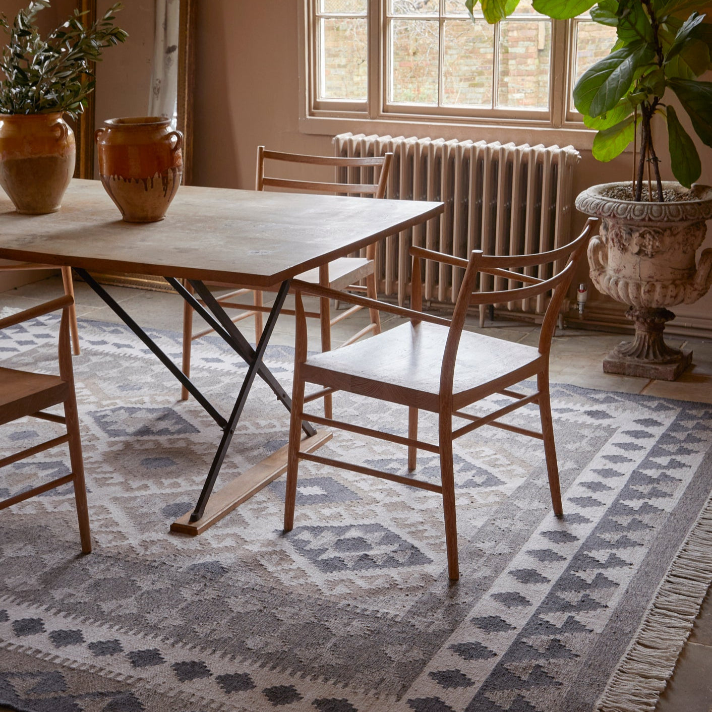 Dining room with wooden table and chairs, large window, and decorative plants.