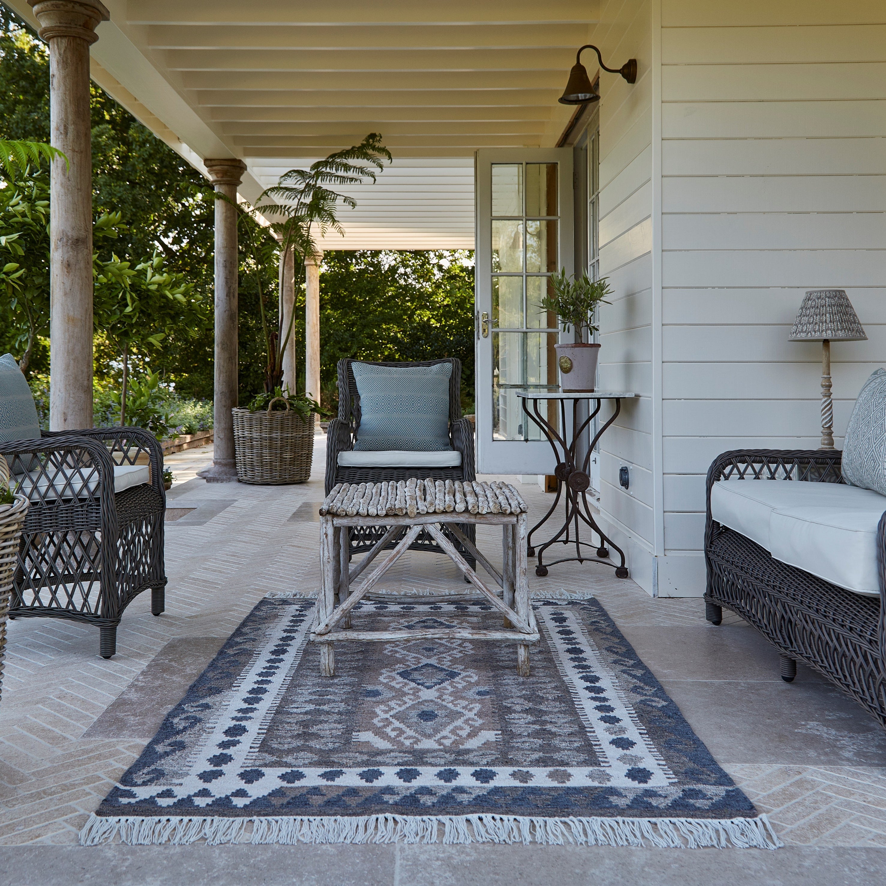Outdoor patio with wicker furniture, rug, and plants on a sunny day.