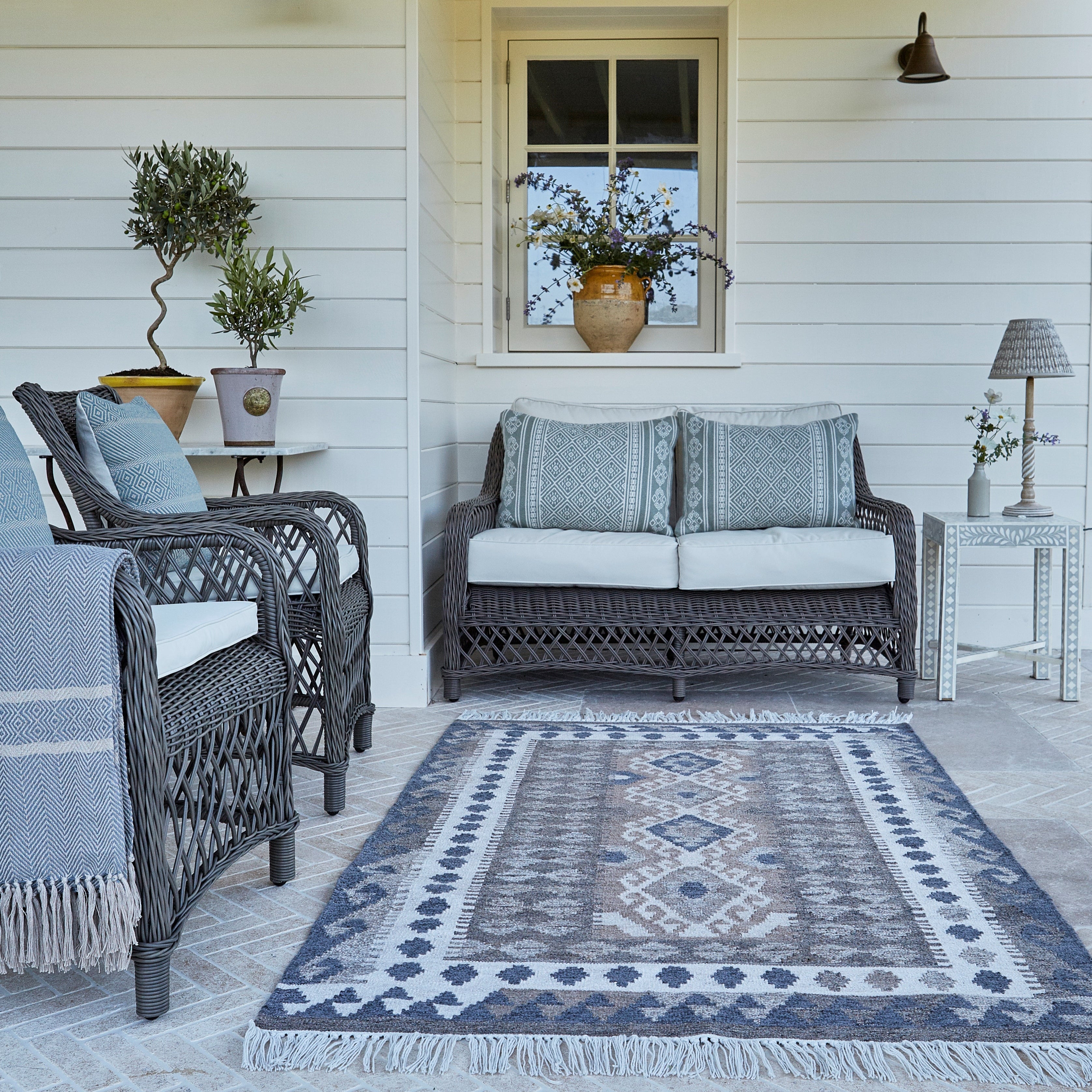 Outdoor patio with wicker furniture, cushions, and a patterned rug on a wooden deck.