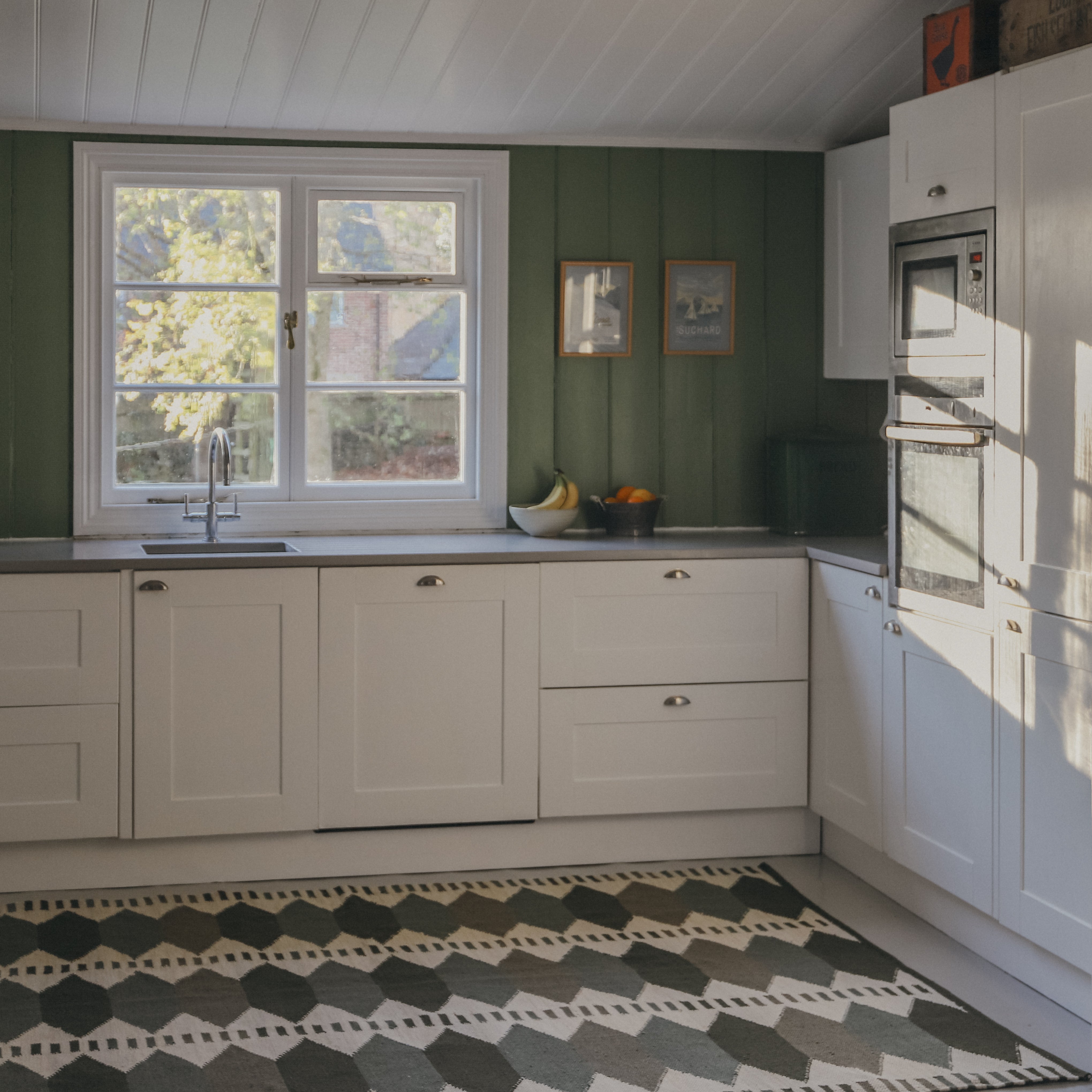 Modern kitchen with white cabinets, green walls, and a green kilim geometric patterned rug.