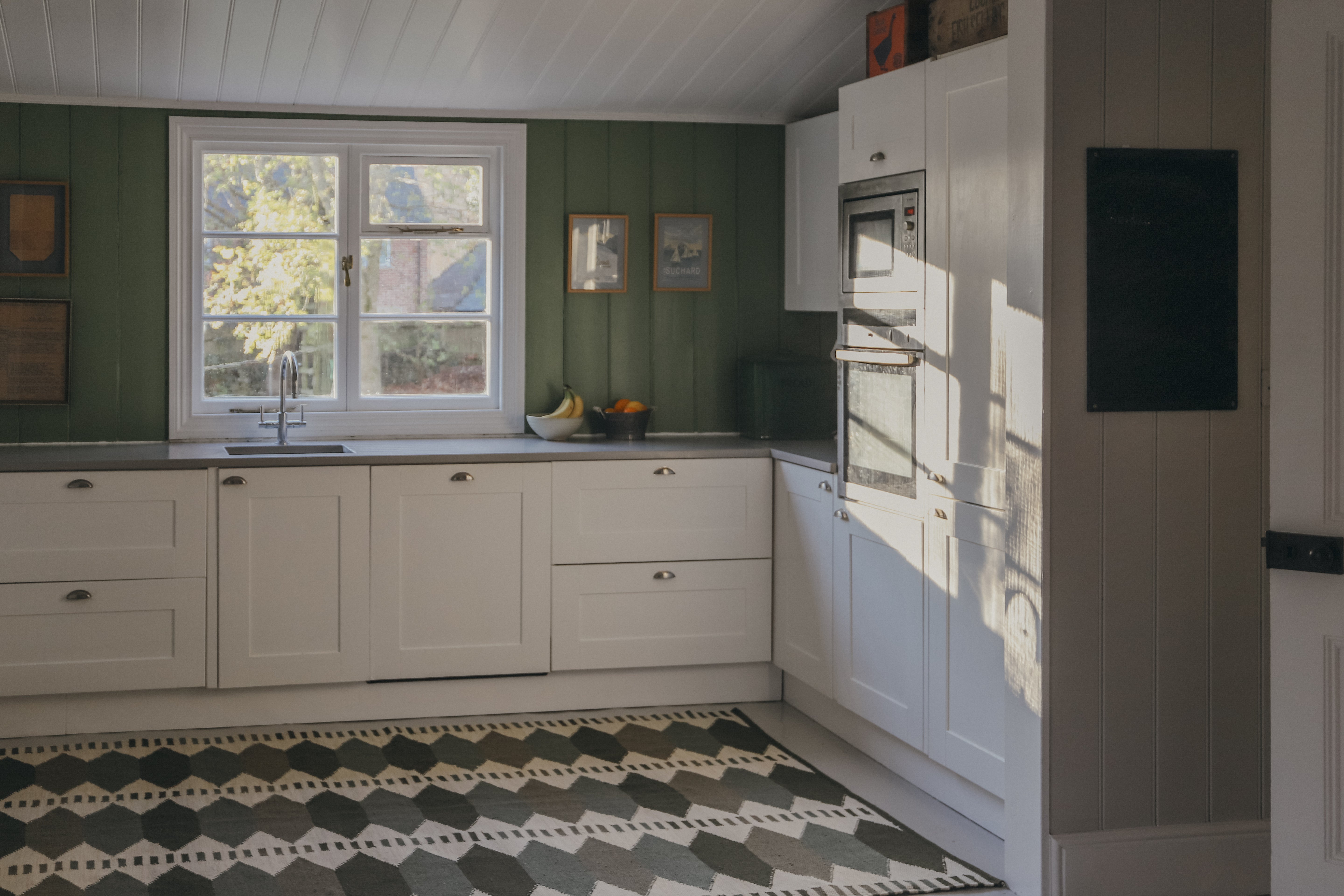 Modern kitchen with white cabinets, green walls, and a green kilim geometric patterned rug.
