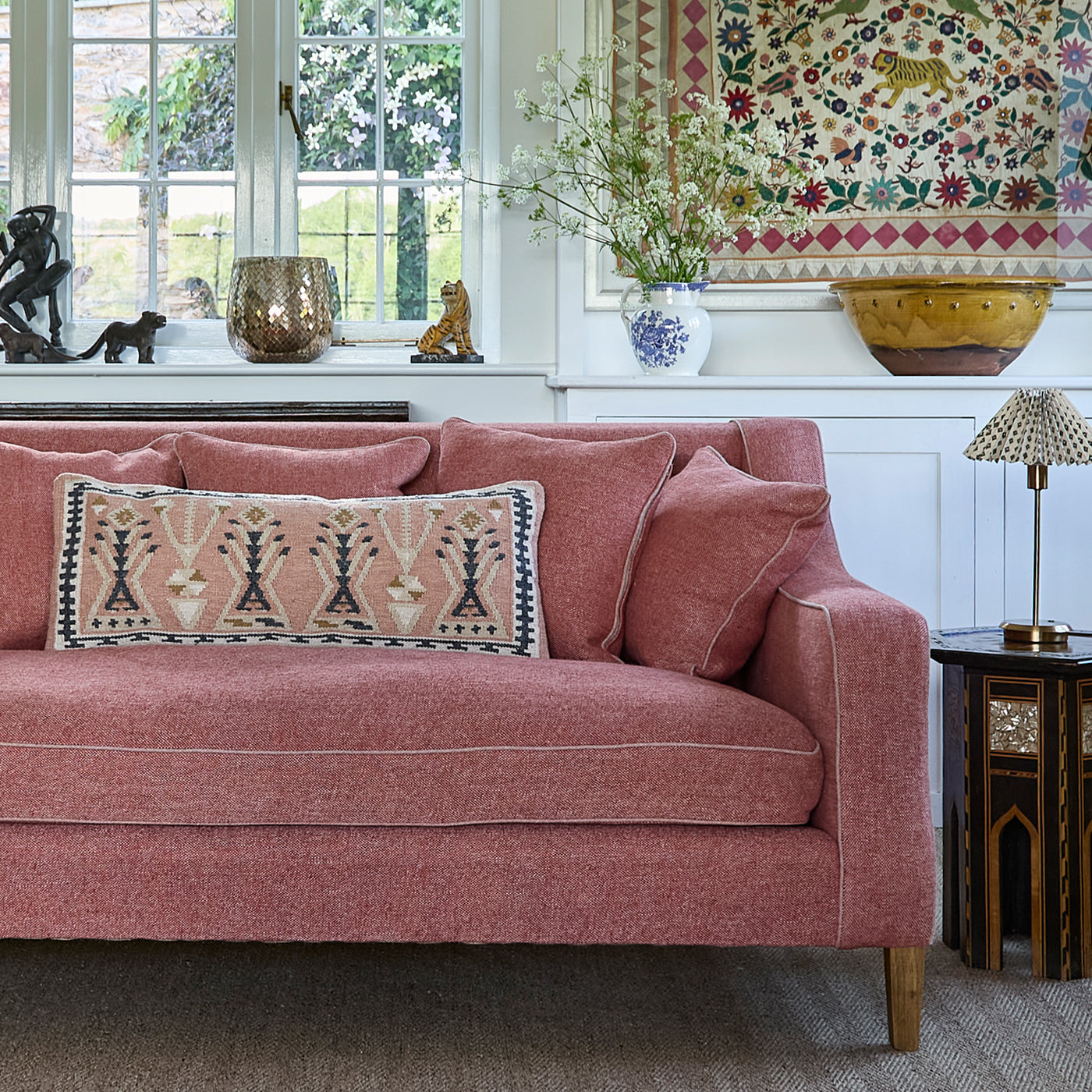 a weaver green aster kilim cushion in a pink and charcoal pattern placed on a pink sofa.