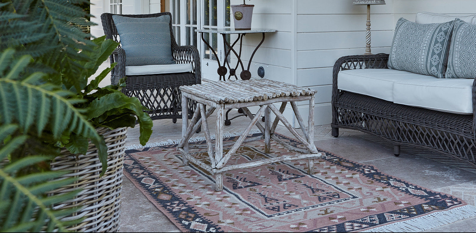 Outdoor patio with wicker furniture, rug, and plants on a porch.