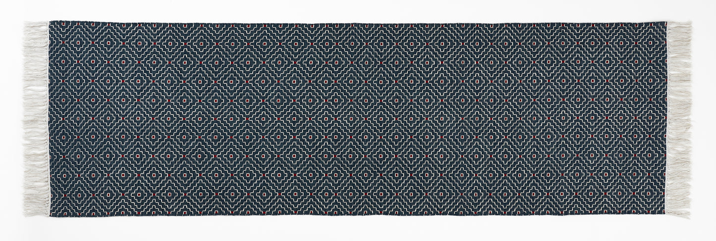 Navy blue woven runner with white geometric pattern and fringes on a white background