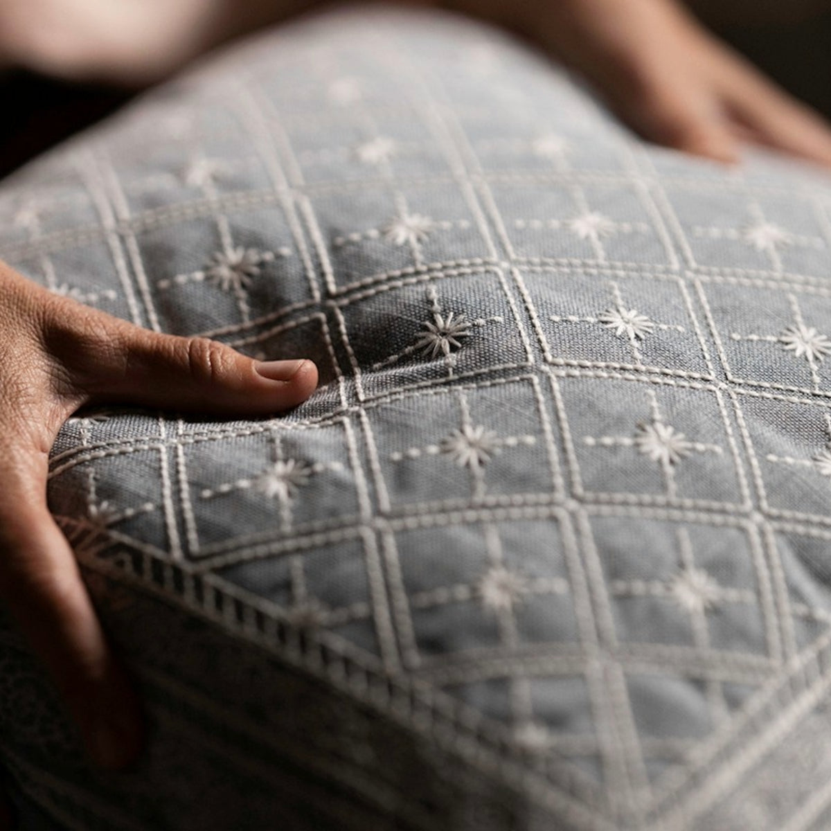 Lucknow Star Weaver Green cushion with white embroidered stars and a hand touching it.