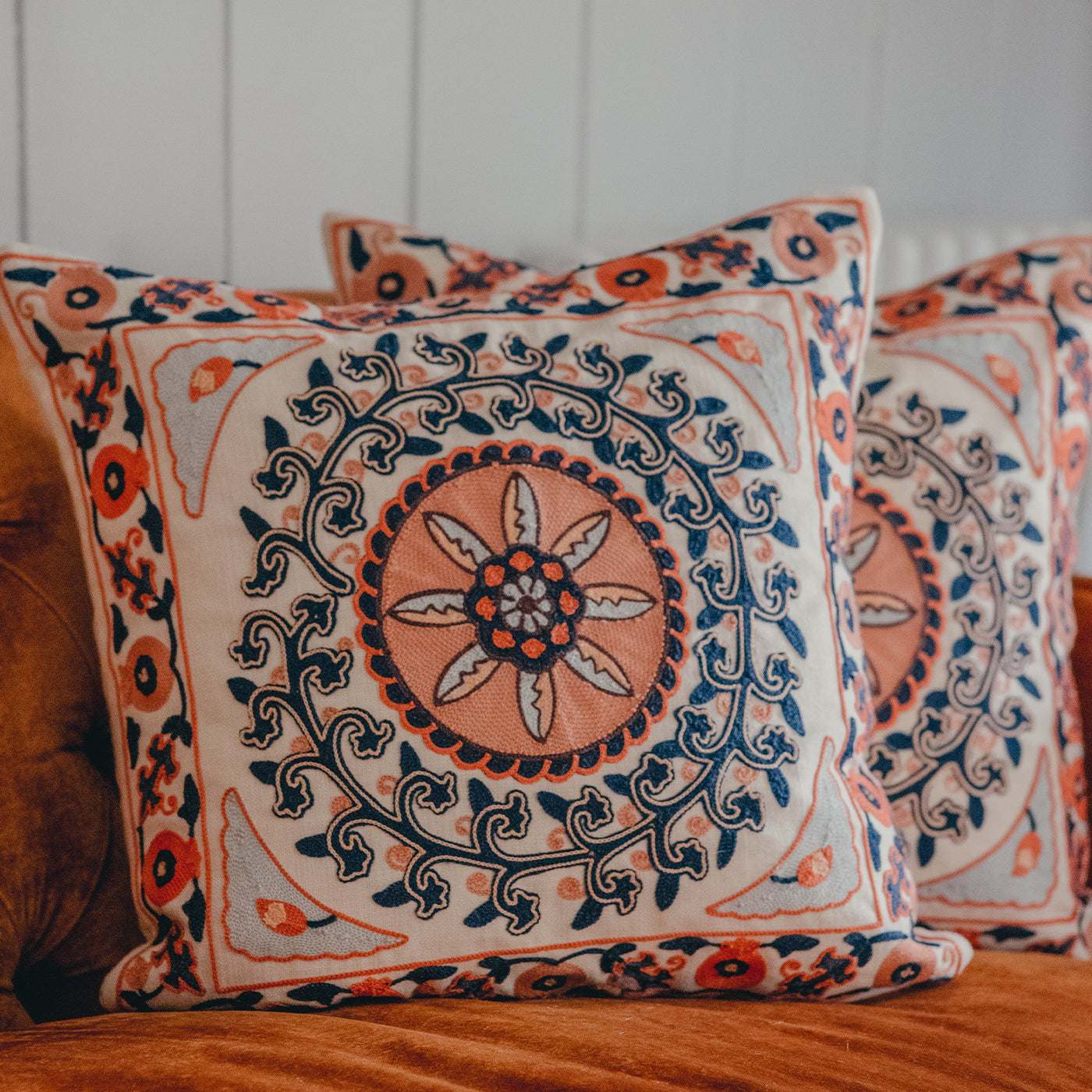 Coral and Navy embroidered cushion on a velvet sofa.
