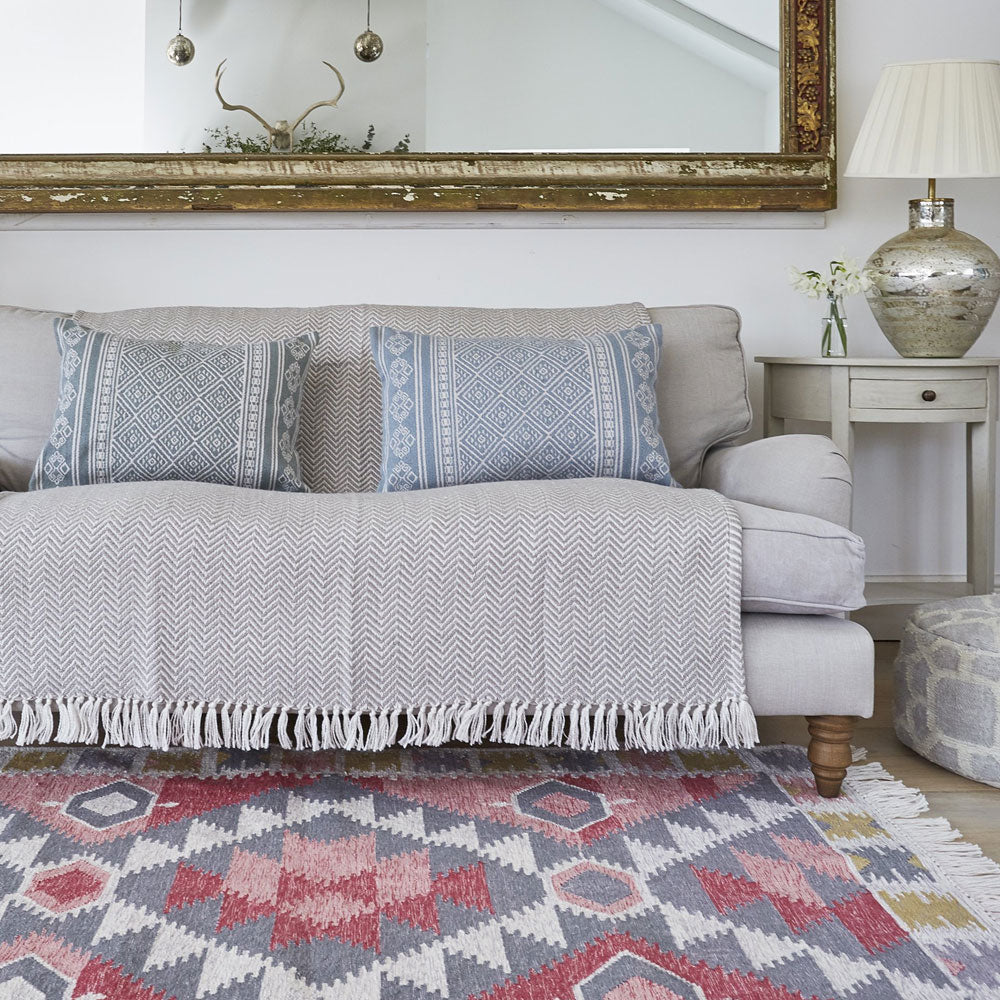 A geometric pink and grey rug with a sofa with cushions and throw in a living room.