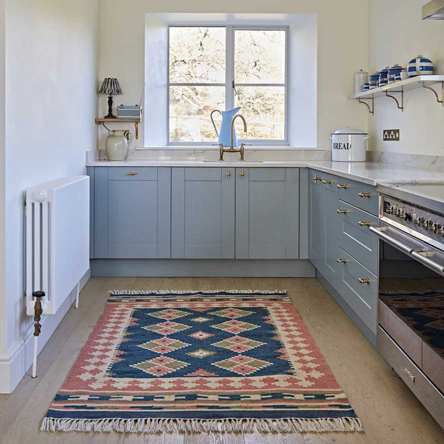 a plaster pink and dark blue geometric rug in a light blue kitchen 